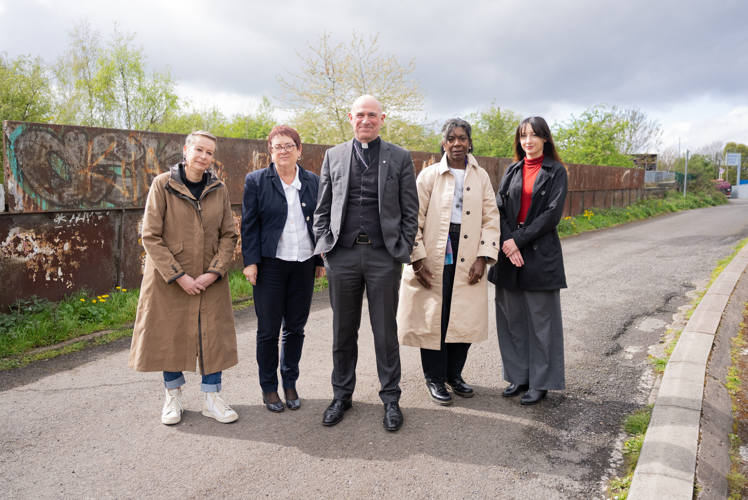 Five members of the Orgreave Chair and Panel stand on a road at the Orgreave site. Pictured left to right are Dr Angie Sutton-Vane, Baroness Mary Bousted, Bishop Pete Wilcox, Wendy Williams CBE and Dr Joanna Gilmore.